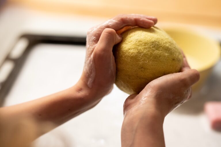 Kinderhände formen eine gelbe Filzkugel beim Nassfilzen