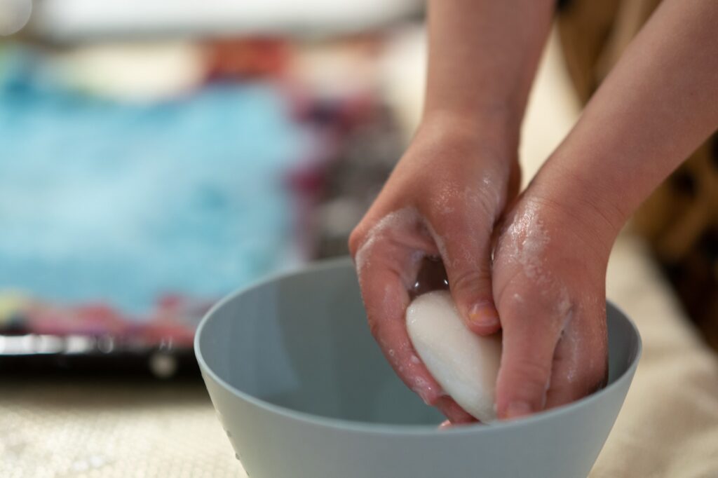 Kinderhände mit Seife über der Wasserschüssel beim Nassfilzen